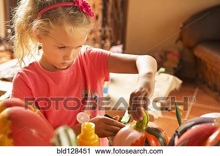 Stock Image - Caucasian girl decorating jack o'lantern. Fotosearch