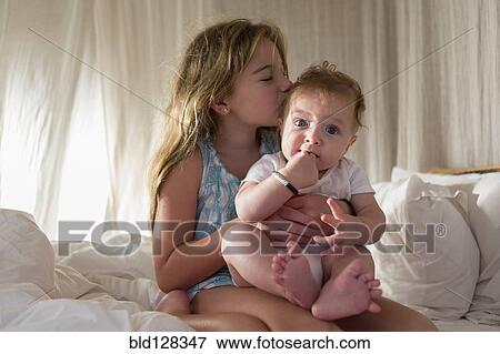 Stock Photo - Caucasian girl kissing sibling on sofa. Fotosearch