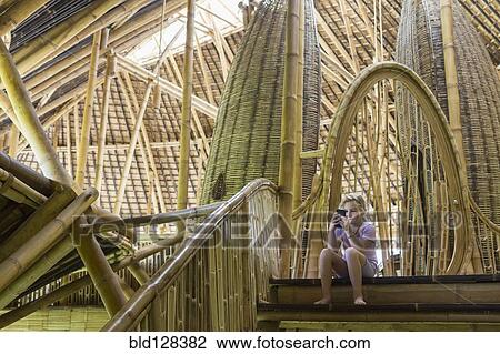 Stock Image - Caucasian girl using cell phone in bamboo hotel. Fotosearch