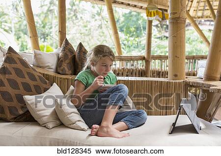 Stock Photography - Caucasian girl watching digital tablet on patio sofa. Fotosearch