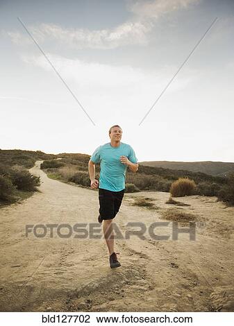 Stock Image - Caucasian man jogging on dirt path. Fotosearch