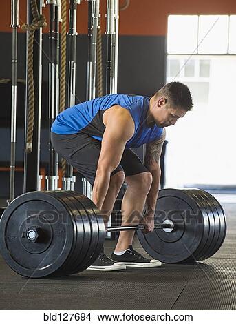 Picture - Caucasian man lifting weights in gym. Fotosearch