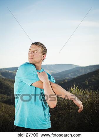 Stock Image - Caucasian man stretching on hilltop. Fotosearch