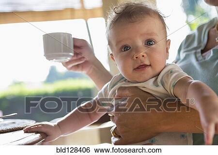 Stock Photograph - Caucasian mother holding baby at breakfast. Fotosearch