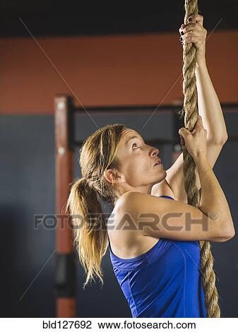 Stock Image - Caucasian woman climbing rope in gym. Fotosearch