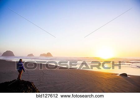 Stock Image - Caucasian woman overlooking sunrise on beach. Fotosearch