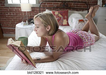 Stock Image - Caucasian woman reading book on bed. Fotosearch