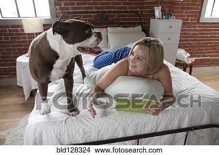 Picture - Caucasian woman relaxing with dog on bed. Fotosearch
