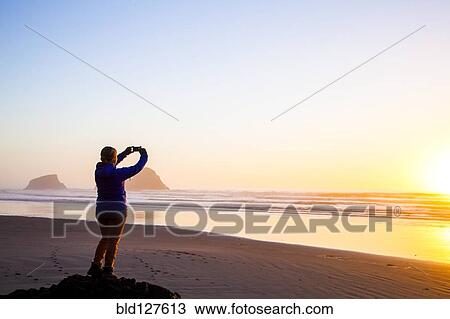 Caucasian woman taking picture of sunrise on beach View Large Photo Image Stock Image - Caucasian woman taking picture of sunrise on beach. Fotosearch