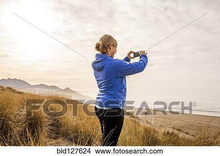 Picture - Caucasian woman taking pictures on beach. Fotosearch