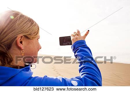 Stock Image - Caucasian woman taking pictures on beach. Fotosearch
