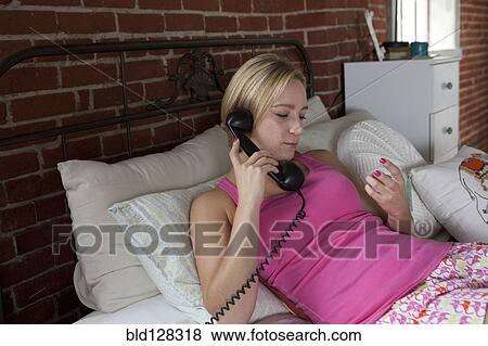 Stock Photo - Caucasian woman talking on telephone in bed. Fotosearch