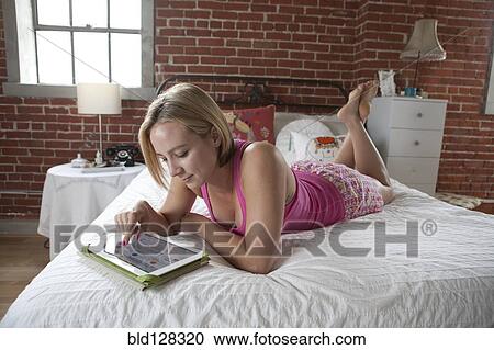 Stock Image - Caucasian woman using digital tablet on bed. Fotosearch