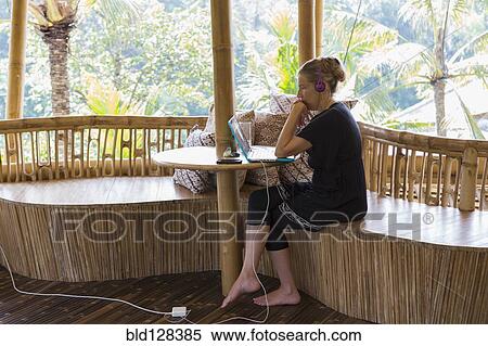 Stock Photography - Caucasian woman using laptop on bamboo patio. Fotosearch