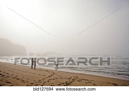 Picture - Couple playing with dog on beach. Fotosearch