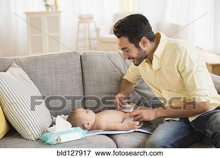 Father changing baby's diaper on sofa View Large Photo Image Stock Photo - Father changing baby's diaper on sofa. Fotosearch