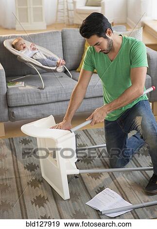 Stock Photo - Father setting up highchair in living room. Fotosearch