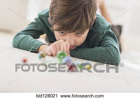 Stock Image - Hispanic boy playing with marbles on bedroom floor. Fotosearch