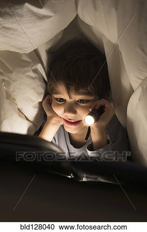 Stock Image - Hispanic boy reading under covers. Fotosearch