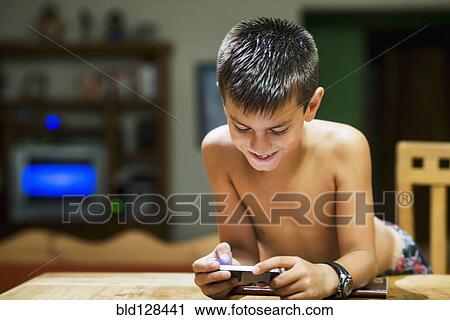 Stock Image - Hispanic boy using cell phone at table. Fotosearch