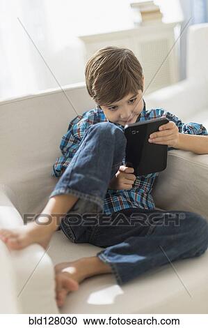 Stock Image - Hispanic boy using digital tablet in armchair. Fotosearch