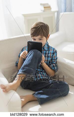 Hispanic boy using digital tablet in armchair View Large Photo Image Stock Photo - Hispanic boy using digital tablet in armchair. Fotosearch