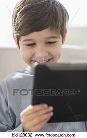 Stock Image - Hispanic boy using digital tablet on sofa. Fotosearch