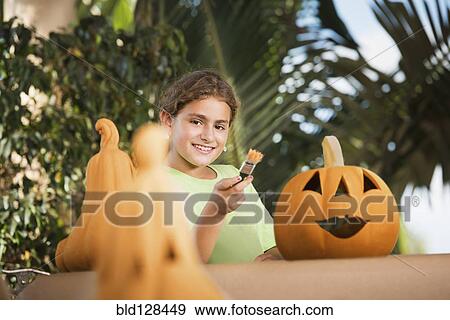 Stock Photo - Hispanic girl decorating jack o'lantern. Fotosearch