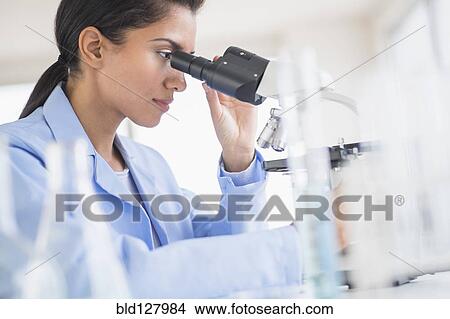 Picture - Hispanic scientist using microscope in laboratory. Fotosearch