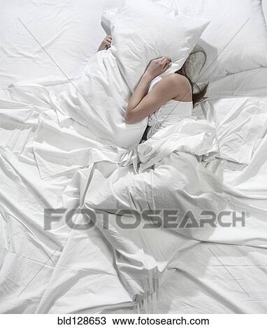 Stock Image - Hispanic woman burying head under pillow. Fotosearch