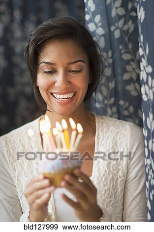 Stock Photo - Hispanic woman looking down at lit candles on birthday cupcake. Fotosearch