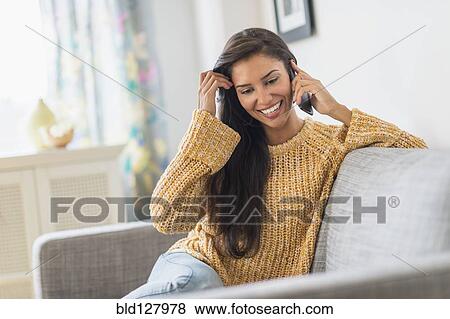 Stock Photo - Hispanic woman talking on cell phone on sofa. Fotosearch