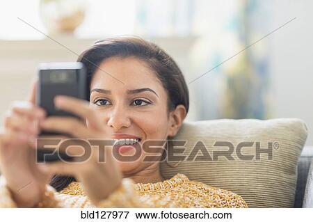 Stock Photo - Hispanic woman using cell phone on sofa. Fotosearch