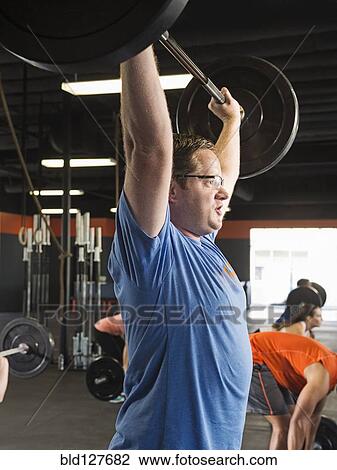 Stock Image - Man lifting weights in gym. Fotosearch