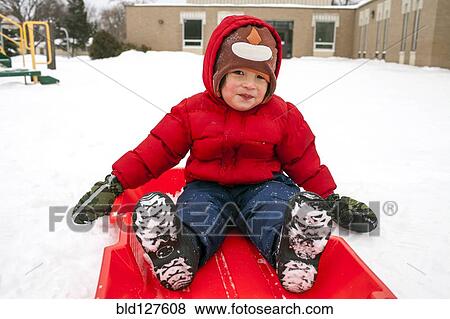 Stock Photo - Mixed race boy sitting on sled in snow. Fotosearch
