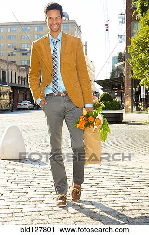 Stock Image - Mixed race businessman carrying flowers on city street. Fotosearch