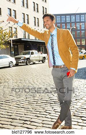 Stock Photograph - Mixed race businessman hailing taxi on city street. Fotosearch