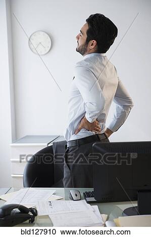 Stock Image - Mixed race businessman rubbing his back in office. Fotosearch