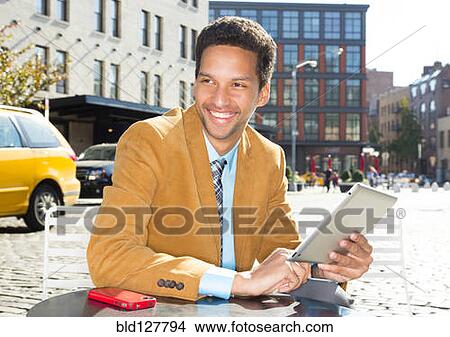 Picture - Mixed race businessman using digital tablet outdoors. Fotosearch