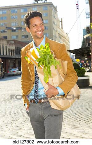 Stock Image - Mixed race businessman with groceries on city street. Fotosearch