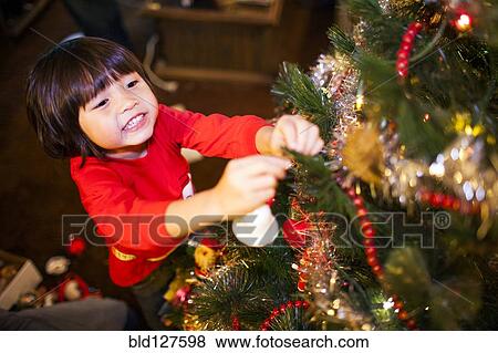 Stock Photo - Mixed race girl decorating Christmas tree. Fotosearch