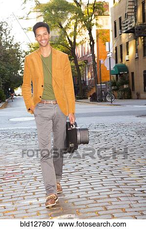 Stock Photo - Mixed race man carrying guitar on city street. Fotosearch