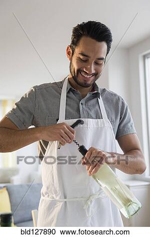 Stock Image - Mixed race man opening wine bottle. Fotosearch