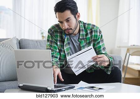 Stock Image - Mixed race man paying bills in living room. Fotosearch