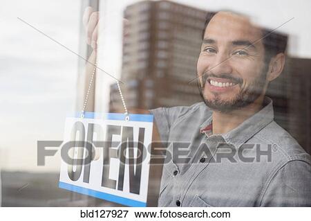 Mixed race man placing Open sign in shop window View Large Photo Image Stock Photo - Mixed race man placing Open sign in shop window. Fotosearch