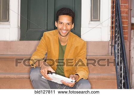 Stock Image - Mixed race man sitting on front steps. Fotosearch