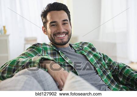Stock Image - Mixed race man smiling on sofa. Fotosearch