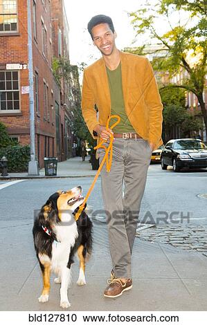 Stock Image - Mixed race man walking dog on city street. Fotosearch