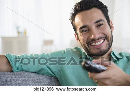 Stock Photograph - Mixed race man watching TV on sofa. Fotosearch
