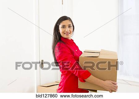 Stock Image - Mixed race woman carrying cardboard box. Fotosearch